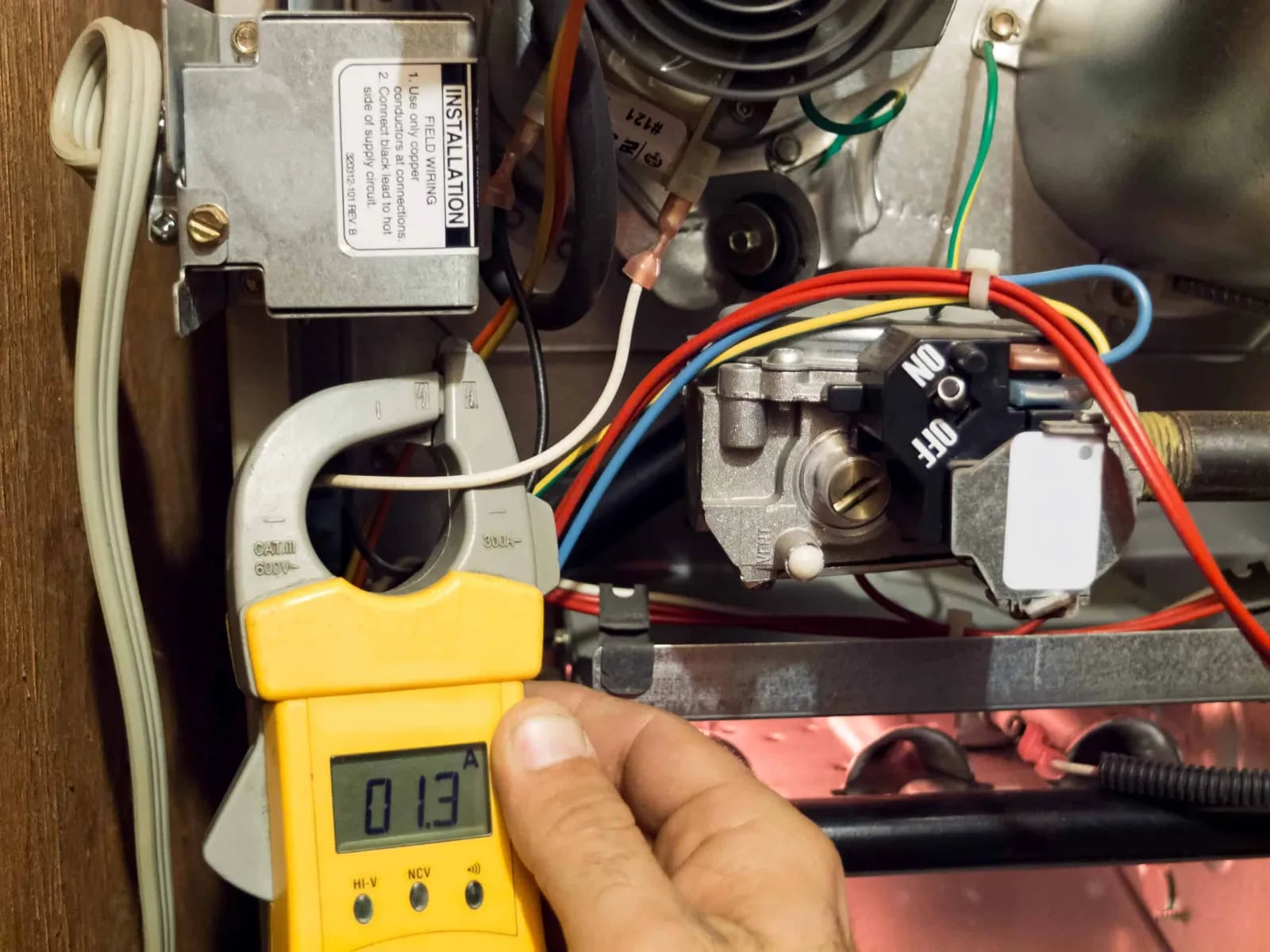Yellow clamp meter reading 0.13 amps on furnace wiring beside the gas valve
